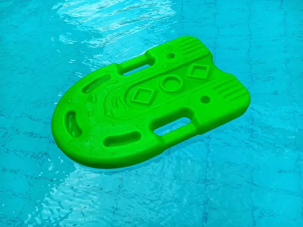 Yüzme havuzunun mavi sularında yüzen yeşil kickboard 'u kapatın. Yüzme öğrenirken kullanılan küçük bir yüzme tahtası.
