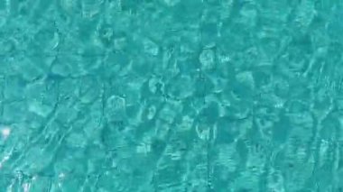 Mavi dalgaların soyut dokusu, arka planda güneş ışığı yansıması olan yüzme havuzunun suyunu dalgalandırır..