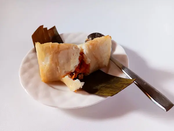 Arem-arem, muz yaprağına sarılmış, içi doğranmış tavuk ve doğranmış sebzelerle dolu, beyaz arka planda izole edilmiş kaşıkla servis edilen Endonezya usulü sıkıştırılmış pirinç keki..