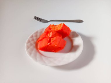 Beyaz arka planda izole edilmiş seramik tabakta taze kesilmiş papaya meyvesi ve çatal..