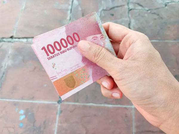 Kadının elinde para var. Yüz bin Endonezya parası. Doğal taşlara izole edilmiş paralar..