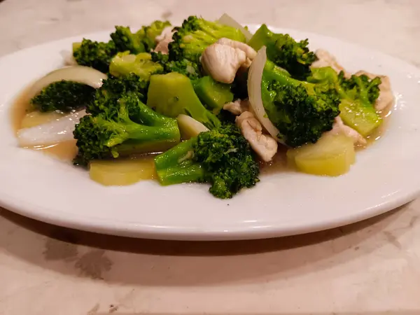 Çin yemeği, tavuk ve brokoli kızartması soğan ve sosla birlikte mermer masada izole edilmiş beyaz bir tabakta..