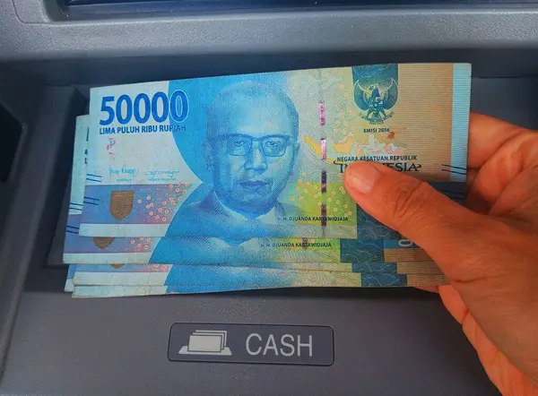Kadın nakit para tutuyor Endonezya rupiası Gri Otomatik Teller Machine (ATM) tarafından izole edilmiş).
