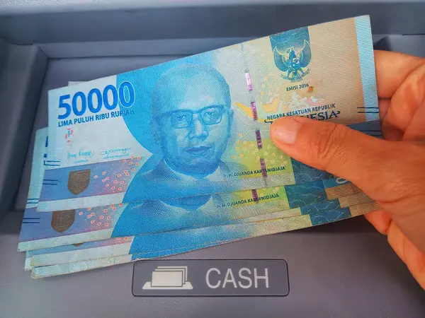 Kadın nakit para tutuyor Endonezya rupiası Gri Otomatik Teller Machine (ATM) tarafından izole edilmiş).