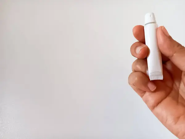 Beyaz arka planda izole edilmiş küçük beyaz tüp diş macunu tutan kadının eli. Metin için alanı kopyala.