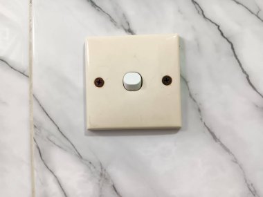 Arka plan olarak mermer desenli duvar fayanslarına karşı kremalı tek elektrik düğmesi.