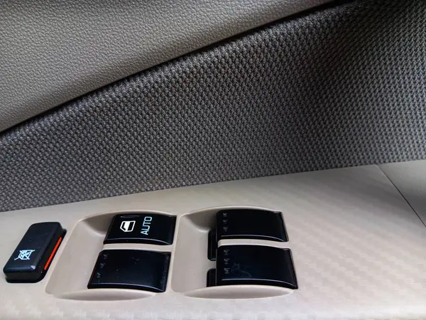 Black windows control button with auto on the driver's side window on a compact sedan car.