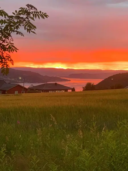 Huzurlu bir günbatımı / gün doğumu sahnesi kırmızı, turuncu, sarı ve pembe renkli bir gökyüzü ile bir köy veya liman kasabası yakınında su yansıtılır, tepeler, tekneler ve bir kırmızı lamba direği huzur verici güzelliğe ilave.