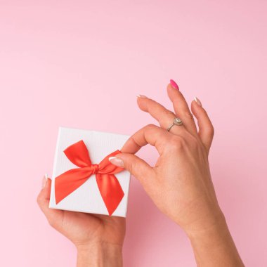 Bir kadının eli pembe arka planda bir Noel hediyesine yağ sürer. Minimum düzlük.