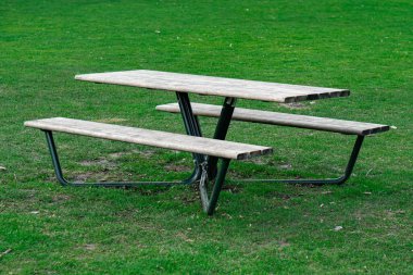 Parkta yeşil çimlerin üzerinde masası olan boş ahşap bir bank.