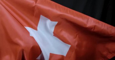 Bu videoda rüzgarda dalgalanan İsviçre bayrağı canlı kırmızı rengini ve açık mavi gökyüzüne karşı ikonik beyaz haçını gösteriyor.