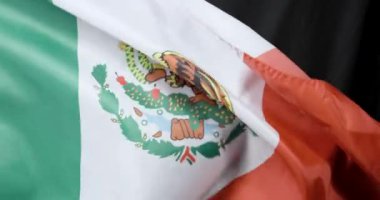 Bu video rüzgarda dalgalanan Meksika bayrağının dinamik hareketini gösteriyor. Kültürü, kimliği ve direnişi simgeleyen siyah bir bayrak ile çelişiyor.