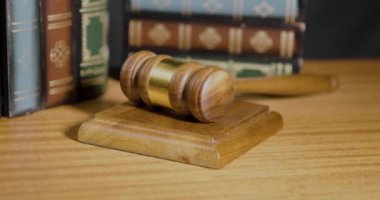 Parlak bir masanın üzerindeki tahta tokmak otoriteyi ve adaleti sembolize eder, bir yığın kitap eşliğinde, yasal tartışmalar için düşünceli bir atmosferi çağrıştırır.
