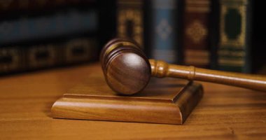 Video, mahkeme salonundaki adalet ve otoriteyi sembolize eden, yasal kitapların önünde, parlak bir masanın üzerinde duran ahşap hakimleri gösteriyor.