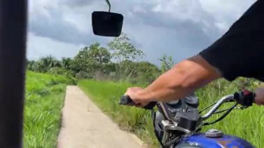 Bir adam engebeli toprak bir yolda motosikletini sürüyor, güzelliğin tadını çıkarıyor yemyeşil yollarda geziniyor, keşfi kucaklıyor.