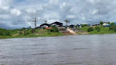 Huzurlu bir nehir sahnesinin güzelliğini yaşayın. Arkaplanda bir vinç ve pitoresk bir bina ile bir kayığın parıldayan suyun üzerinde süzülüşünü.