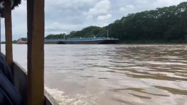 Küçük bir teknenin suda yüzmesi ve dalgalanmalar yaratması gibi doğanın güzelliğini deneyimlemek. Uzakta, büyük bir gemi yelken açar, sakin bir kontrast yaratır.