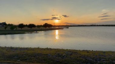 Güneş sakin bir göl üzerinde batarken, sular sıcak akşam gökyüzünü yansıtır. Resimli bir iskele çarpıcı günbatımını çerçeveler, güzellikleri yakalar.