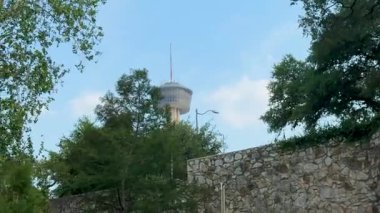 Bu videoda geniş bir ağacı, büyüleyici bir su kulesi ve karmaşık taş duvarları olan yemyeşil bir park, mavi gökyüzü ile ahengi vurguluyor.