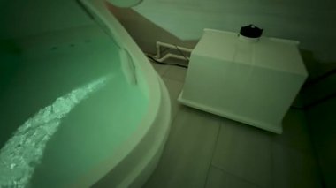 Esrarengiz bir banyo, ürkütücü yeşil su ve yakınlardaki bir kutuyla dolu beyaz bir küvet içeriyor ve izleyicilerin ilgisini çeken bir dünya dışı sahne yaratıyor.