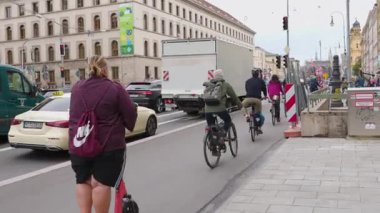 Münih, Almanya 20 Temmuz 2025: Bu şehir videosu şehir enerjisini yansıtan çeşitli ulaşım bisikletçileri, elektrikli scooter kullanan kadınlar ve yayalarla dolu canlı bir caddeyi gösteriyor