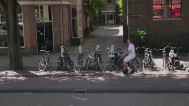 Bu video, park halindeki bisikletlerle, şehir yaşamını ve toplumsal bütünleşmeyi gösteren kaldırımda bisiklet süren insanların olduğu canlı bir şehir sahnesini içeriyor.