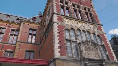 Bu video, güneşli bir günde saat kulesi olan, çok sayıda pencere, kemer ve kırmızı tente içeren çarpıcı bir kırmızı tuğla bina sergiliyor.