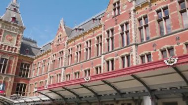 Bu video, birçok penceresi olan büyük kırmızı tuğla bir bina ve bir heykel ve şık bir kırmızı tente ile aydınlatılmış zarif bir saat kulesi içerir.