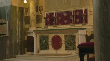 Güzel süslenmiş bir kilisede sakin bir atmosferde titreyen mumlar ve görkemli bir haçla aydınlatılmış büyüleyici bir mermer sunak bulunur.