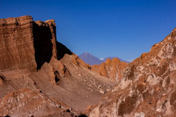 stock image Giant ochre-colored mountains in the Atacama Desert where a volcano can be seen in the background