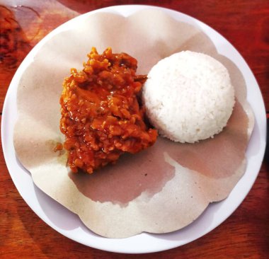 Bir tabak soslu kızarmış tavuk ve bir porsiyon pirinç. Tabaklar ahşap bir masada servis edilir..