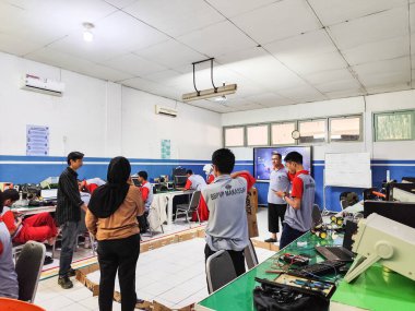 Makassar, 5 Nisan 2024 - Teknik bir sınıfta robotik ve elektronik projeleri uygulayan öğrenciler, arka planda bir öğretmen denetimi ve beyaz tahta notları ile.