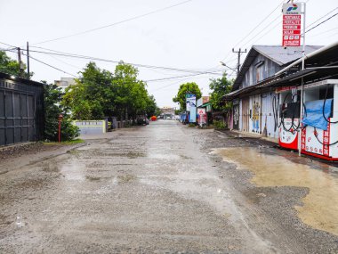 Wajo, 10 Nisan 2024 - Yağmurdan sonra Endonezya 'da sakin bir köy yolu, yol boyunca küçük benzin istasyonları ve küçük dükkanların yer aldığı.