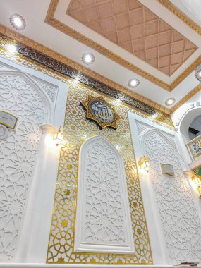 Wajo, 10 Nisan 2024 - Caminin karmaşık duvarları, altın İslami geometrik desenlerle çevrili ve sıcak ortam ışıklarıyla aydınlatılmış Arap kaligrafisinde Allah sözcüğünü içerir..