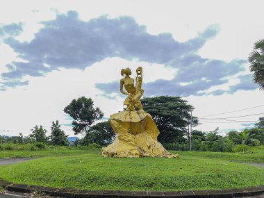 Dansçı bir çifti betimleyen altın bir heykelin arka görüntüsü kayalık bir kaidede, yemyeşil bir çayırda..