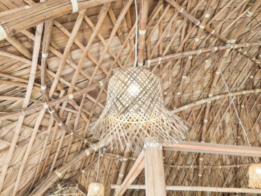 El yapımı bambu kolye lambası, dokuma bambu tavandan sarkıyor, doğal dokuları ve kırsal iç tasarımı vurguluyor..