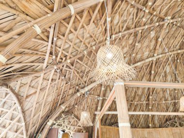 El yapımı bambu kolye lambası, dokuma bambu tavandan sarkıyor, doğal dokuları ve kırsal iç tasarımı vurguluyor..