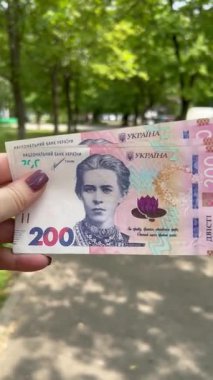 Yeşil bir caddenin arka planına karşı Ukrayna ulusal para birimi bir kadının elinde.