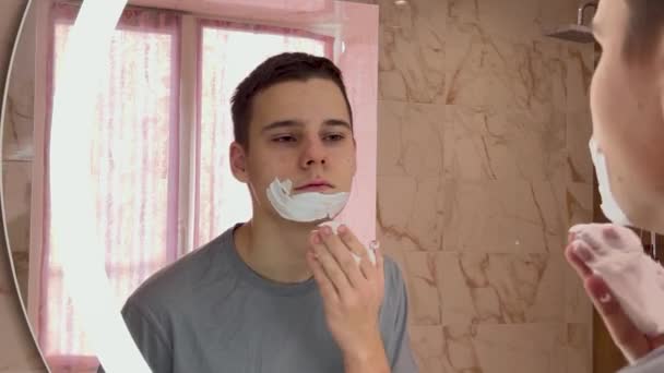 Bonito Adolescente Aplicando Creme Barbear Seu Rosto Enquanto Olha Espelho — Vídeo de Stock