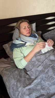 Hasta sarışın kadın yatakta, mendille hapşırıyor. Soğuk virüs belirtileri: baş ağrısı, hijyen odaklanma. Sağlık / İlaç temaları: hasta rahatsızlığı, iyileşme.