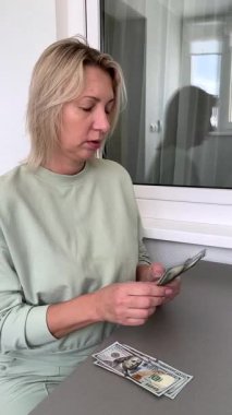 Orta yaşlı sarışın bir kadın bir masada oturmuş dolarları sayıyor ve onları bir sürü yığına koyuyor. Yeteri kadar parası olduğu ve hayallerindeki gibi gülümsediği için mutlu..