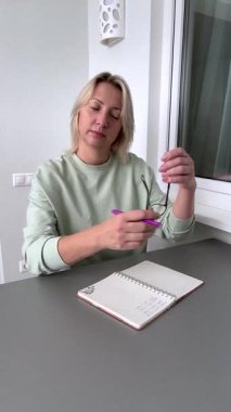 Evde çalışan yetişkin bir kadın, defter başında şaşı, düzeltici gözlük takıyor, odaklanarak yazmaya devam ediyor. Yaşla ilgili görme sorunları için görme sorunu çözme, el yazısı konsantrasyonu, iş verimliliği