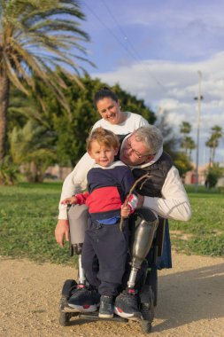 Bir aile, babalarının iyileşmesi için iki bacağı kesilmiş ve tekerlekli sandalyede mutlu bir şekilde poz verir..