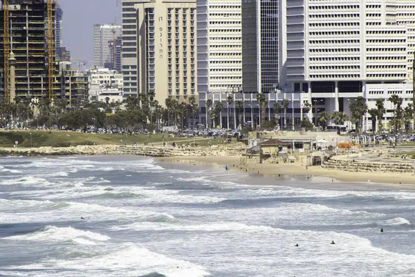 Dalgalar Tel Aviv Sahili 'ne çarpar. İnsanlar kumsalda eğlenir, sörfçüler yakalar dalgaları ve güneşi.