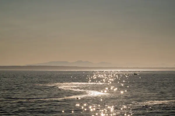  Denizin üzerinde gün batımı, suda yansıma ve arka planda dağ.