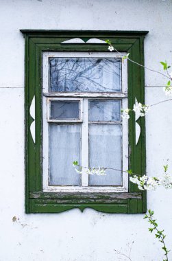 Terk edilmiş bir evin beyaz duvarında bahar çiçekleri olan eski ahşap bir pencere.