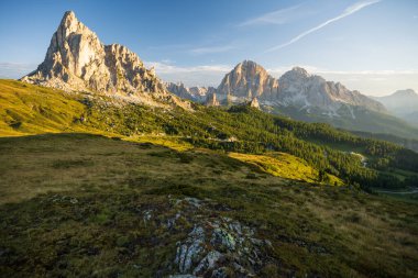 Sunrise at Passo Giau with road and parked cars and campers with sun shining at meadow and peaks during summer morning in august clipart