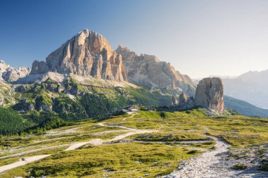 Cinque Torri peaks and Tofane Mountains in Italian Dolomites at summer cloudless morning with green grass lighteen by warm light of sun from right side and path inf front clipart