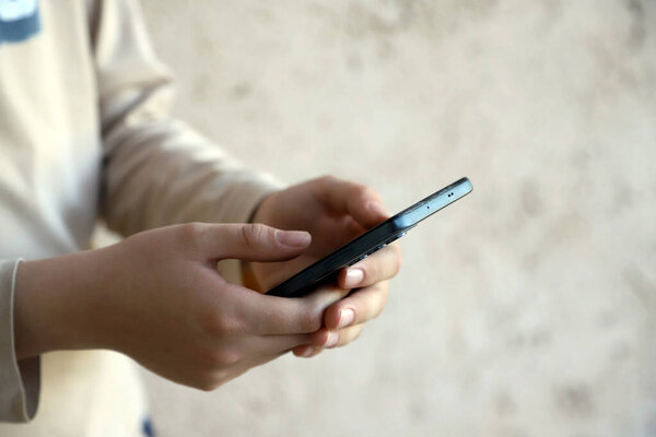 Child's hands playing on his cell phone. Teenager using social networks on his smartphone. Child connected to technology. Light background with copy space.