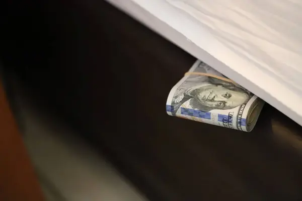 Person keeping money under the mattress. Person hiding their savings in their home. Hand keeping wad of dollar bills on his bed. Concept of distrust in banks and financial entities.
